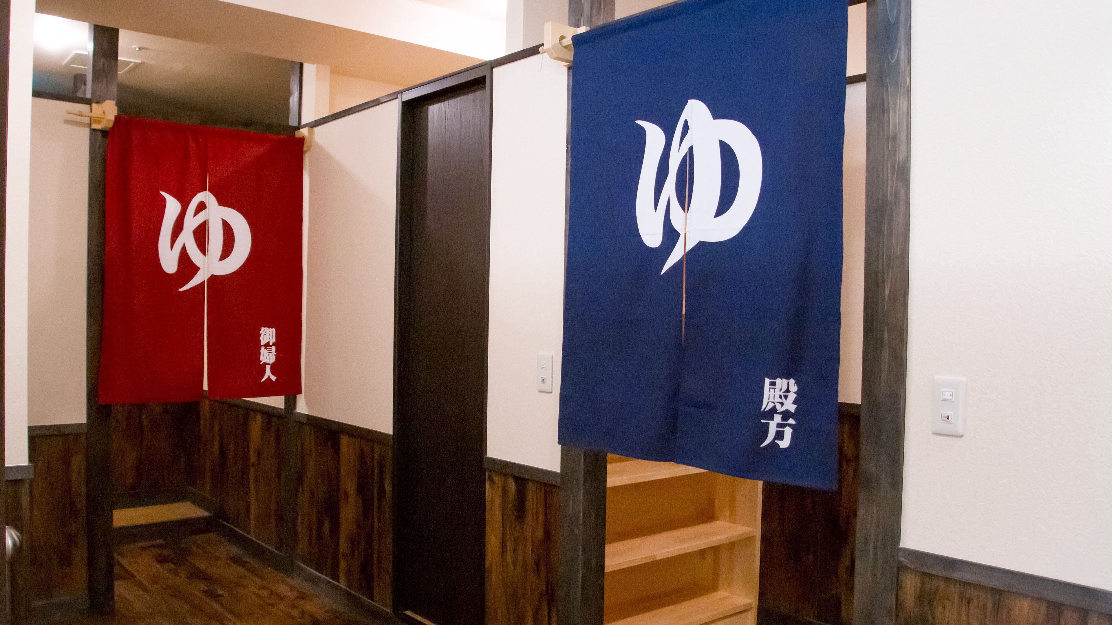 A hallway with wooden flooring and a staircase. There are two banners hanging on the wall, one red and one blue, with white text and symbols.