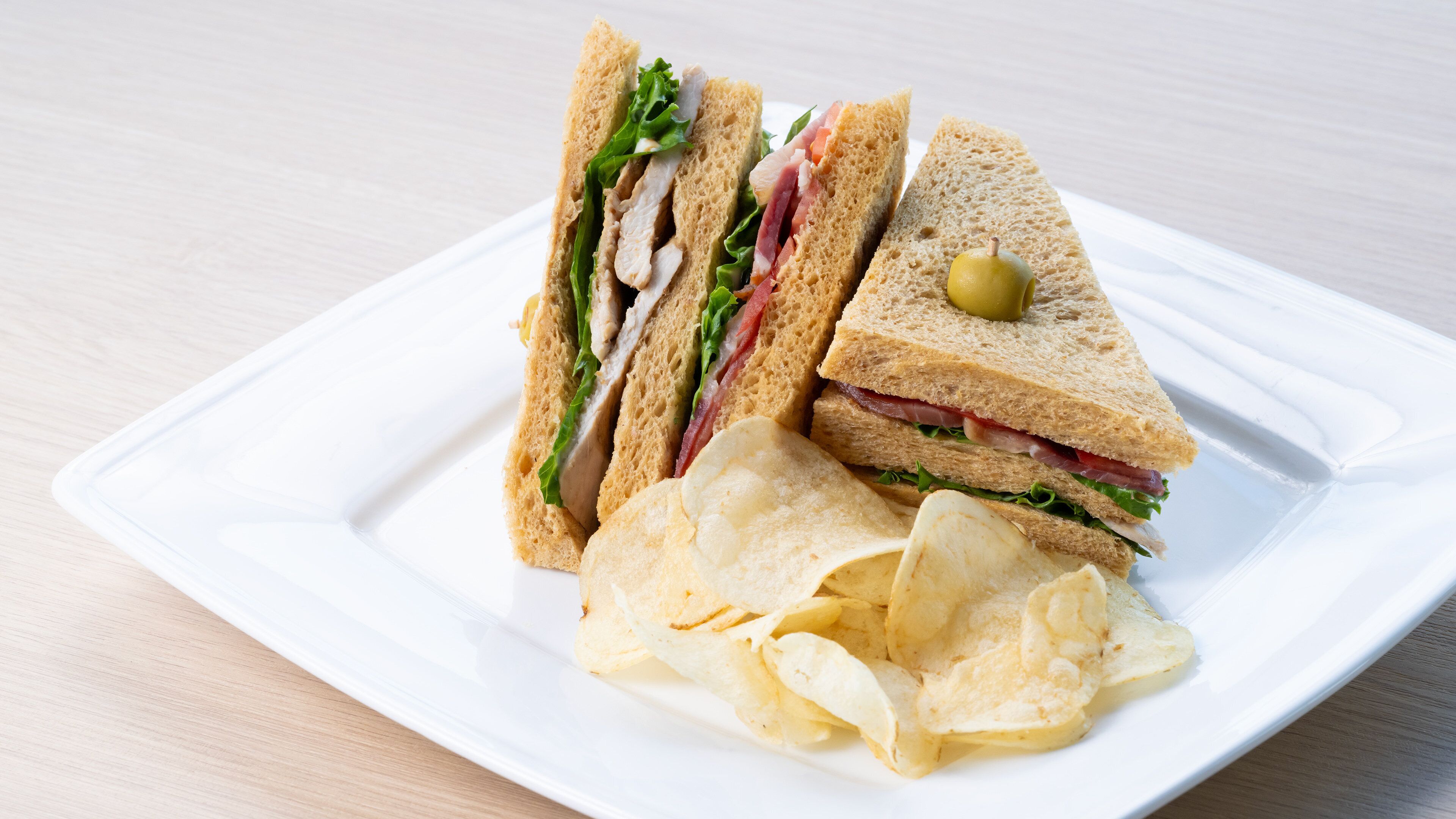 A sandwich with lettuce, tomato, and a slice of cheese, accompanied by a small bowl of chips on a white plate.
