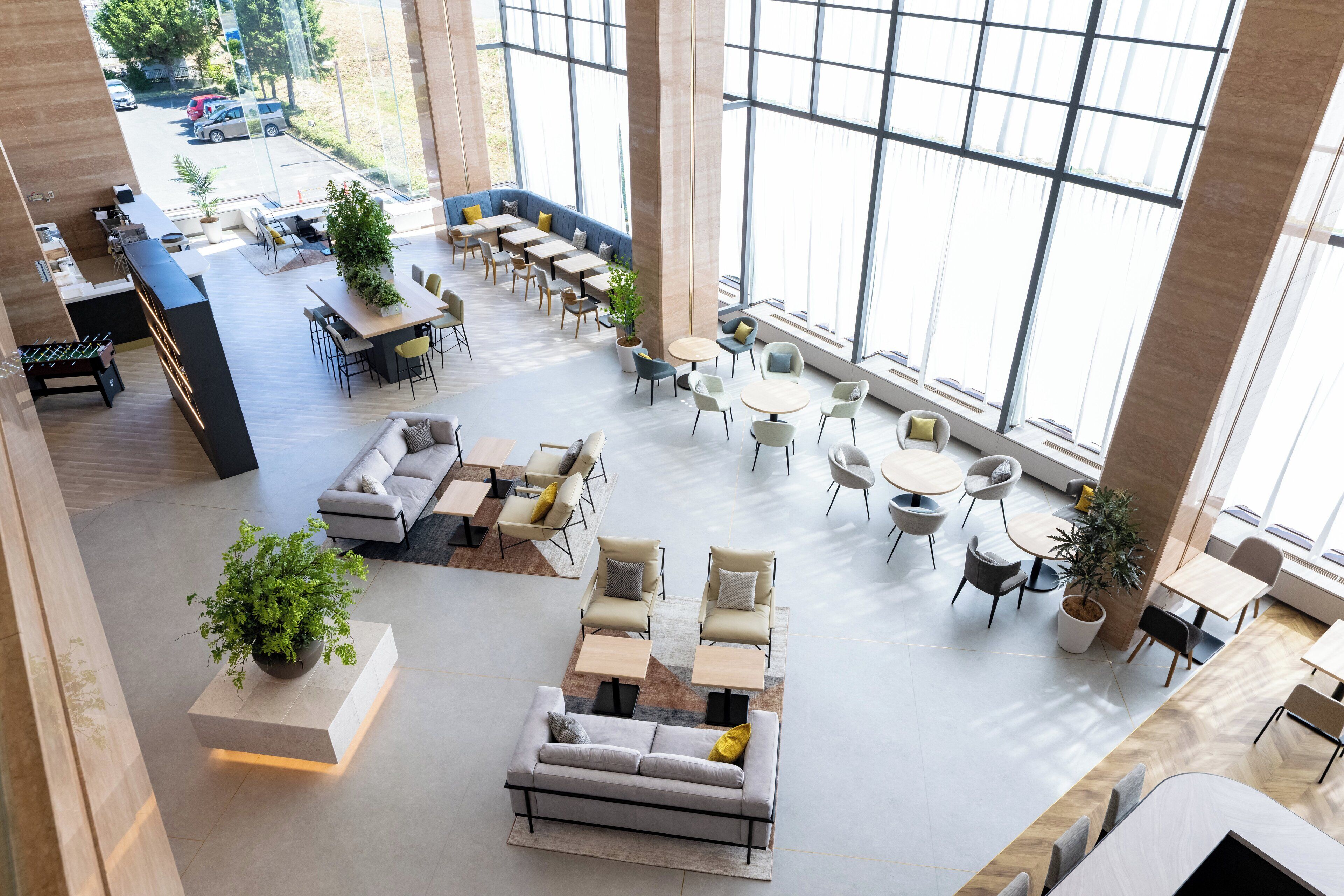 A spacious indoor area with multiple seating arrangements, including sofas, chairs, and tables. There are large windows providing natural light and a view of the outside.