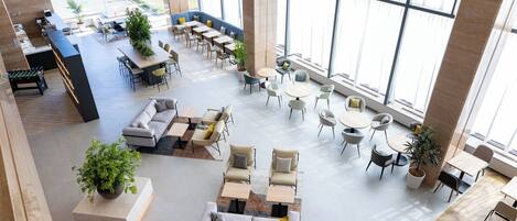 A spacious indoor area with multiple seating arrangements, including sofas, chairs, and tables. There are large windows providing natural light and a view of the outside.