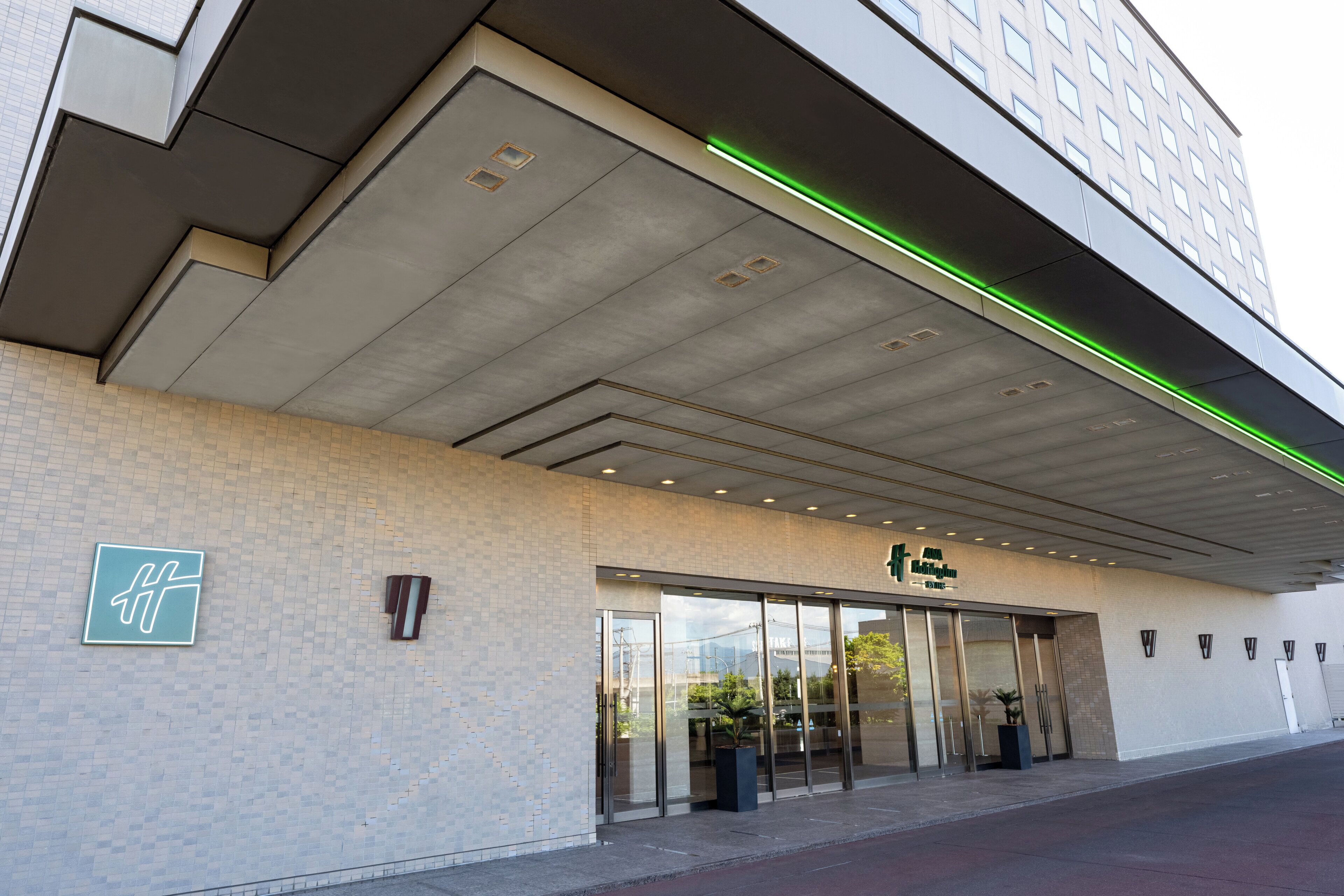 A hotel entrance with a modern design, featuring a large glass door and a sign with a stylized 'H' logo.