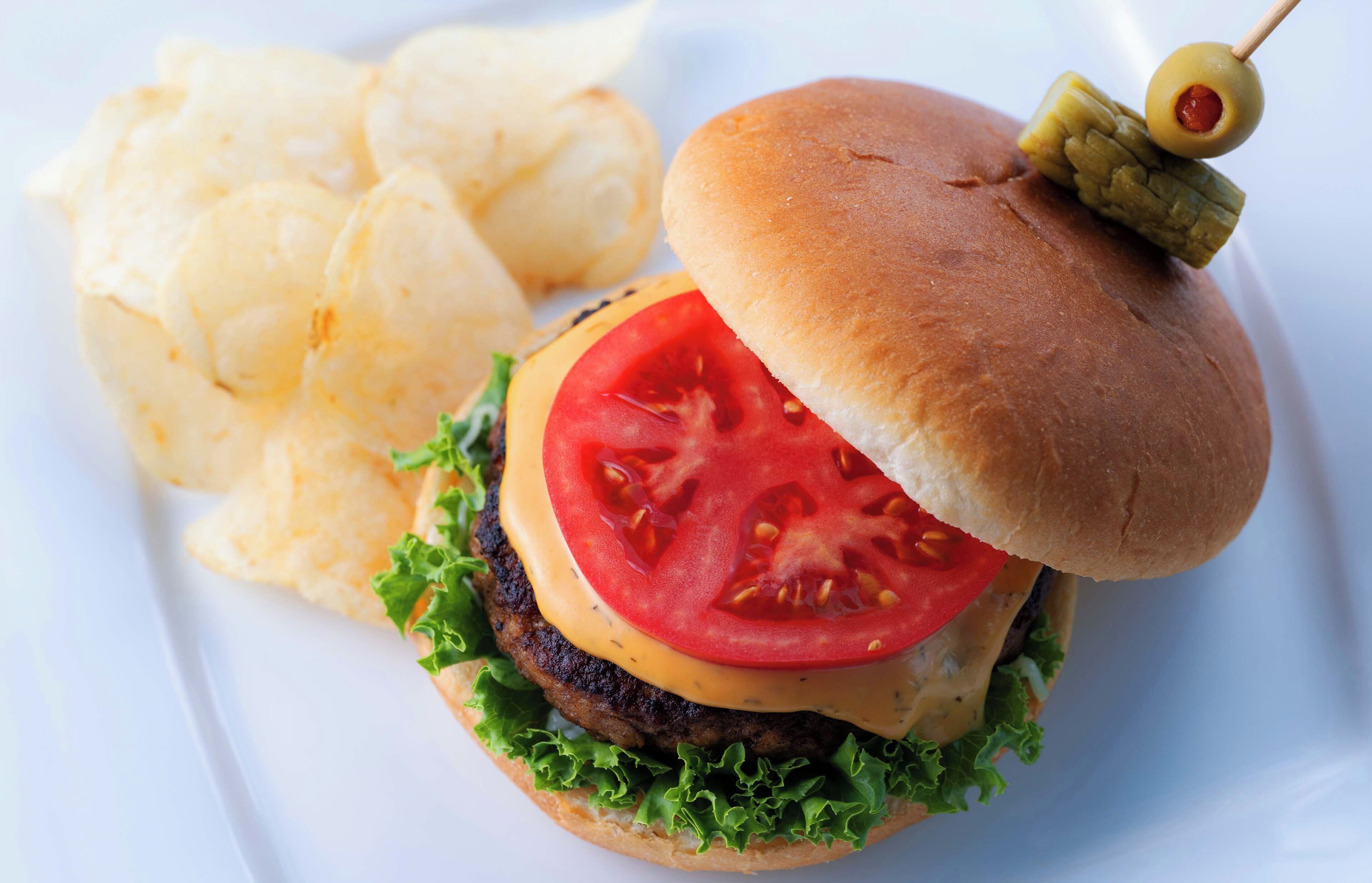 Ein Hamburger mit Tomatenscheibe, Salat und Käse, dazu Kartoffelchips.