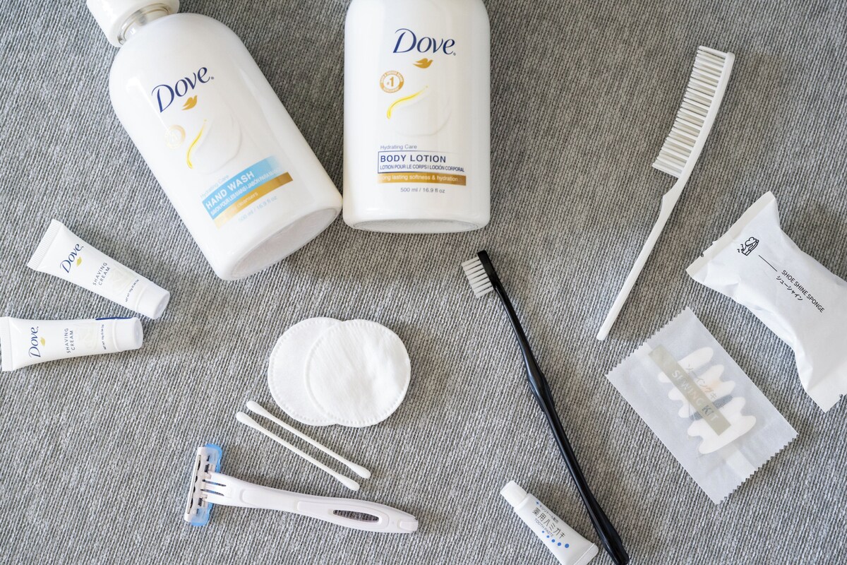 Dove body lotion, hand wash, shaving cream, razor, and other grooming items laid out on a textured surface.