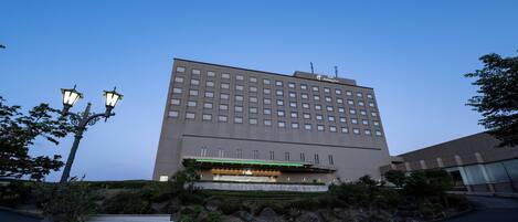 En stor, rektangulär byggnad med ett platt tak och många fönster. Framför byggnaden finns en skylt med texten ”ANA Holiday Inn” och ”Iwataki Kitakami”.