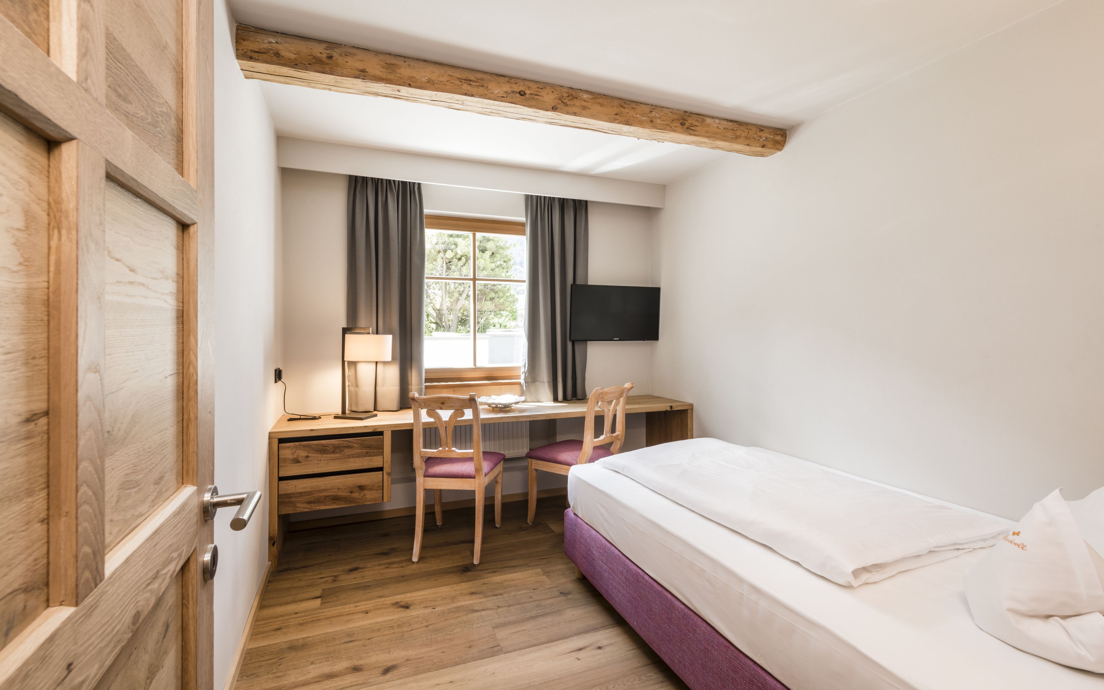 A compact room with a wooden desk, a bed, and a TV.