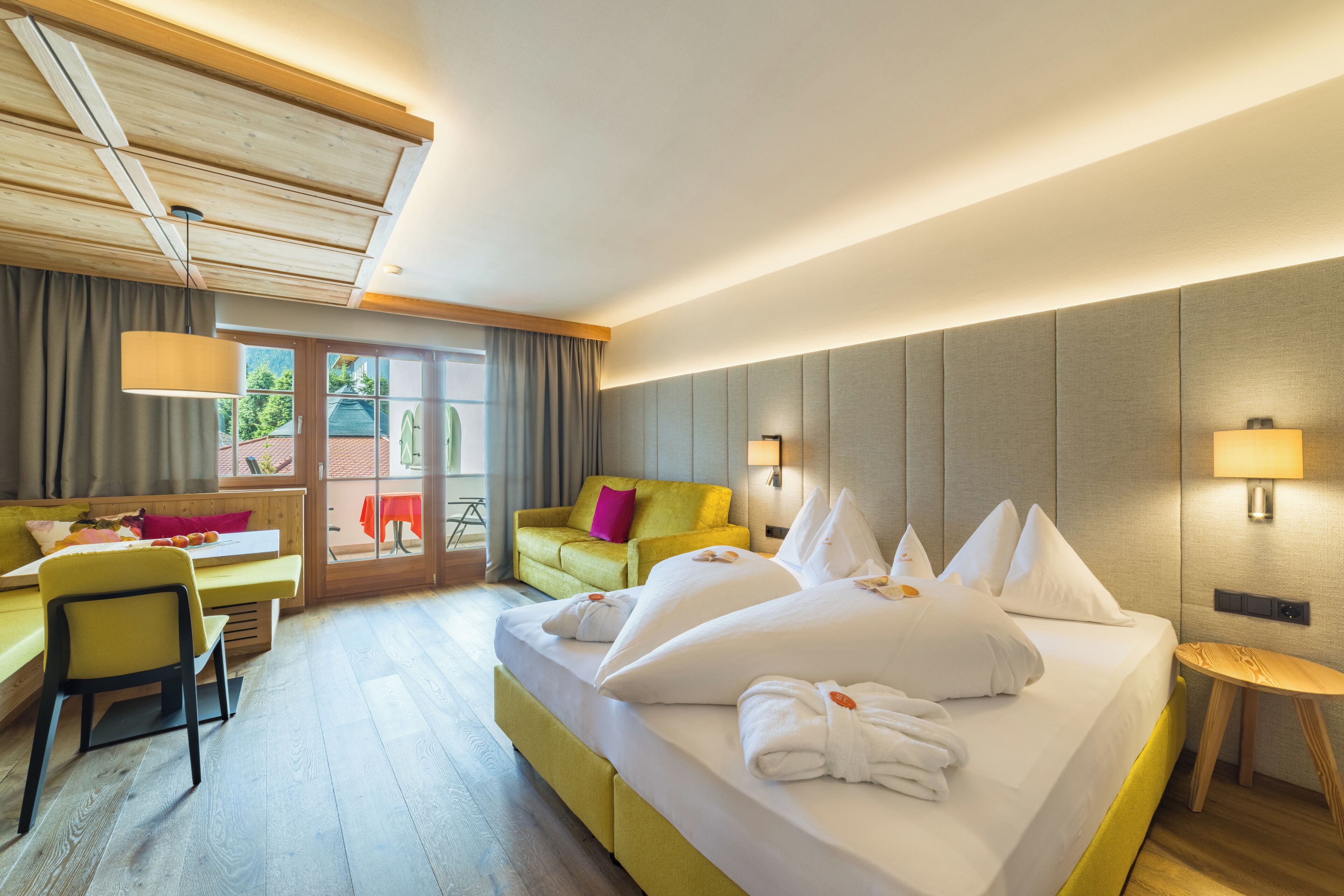 A hotel room with a bed, a sofa, a desk, and a window with curtains.