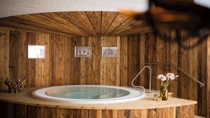 Un interior de madera con un jacuzzi circular, cuadros en la pared y un pequeño florero con flores sobre un mostrador de madera.