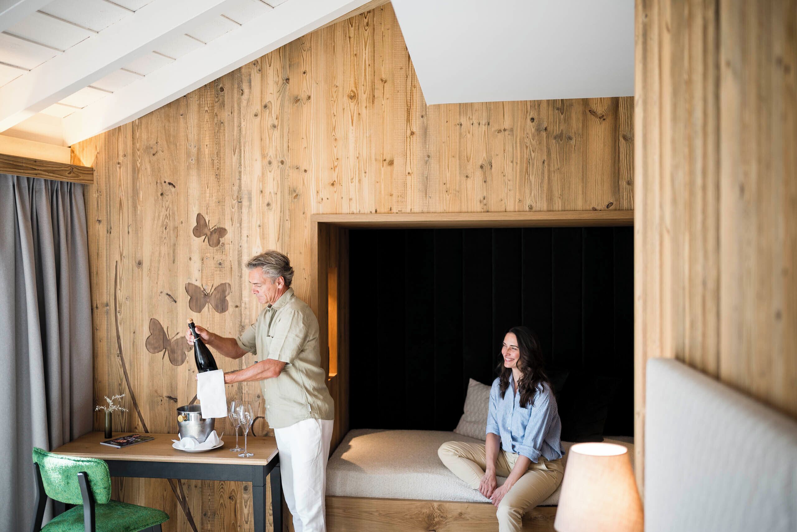 A room with wooden paneling, a sofa, a table with a bottle of champagne, and a green chair.