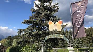 A golf club entrance with a butterfly sign, a flag, and a sign indicating a golf course.