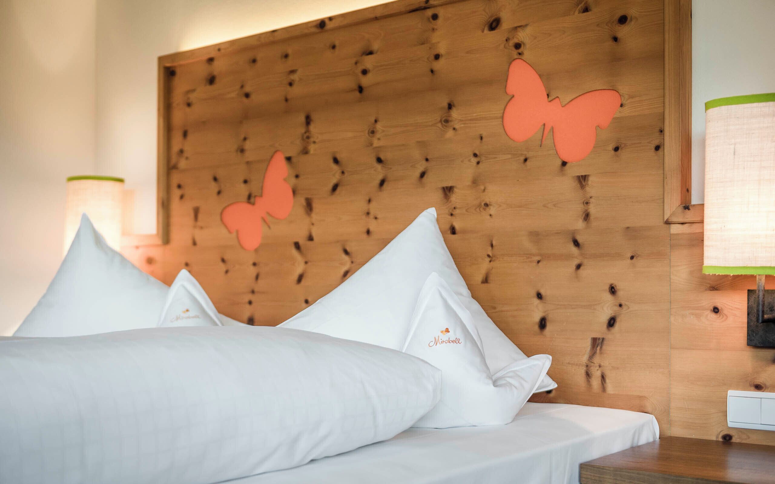 A hotel room with a wooden headboard, white bedding, and decorative butterfly cutouts.