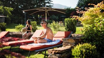 Zwei Sonnenliegen in einem Garten mit Steinmauer, umgeben von viel Grün und einer Pergola.