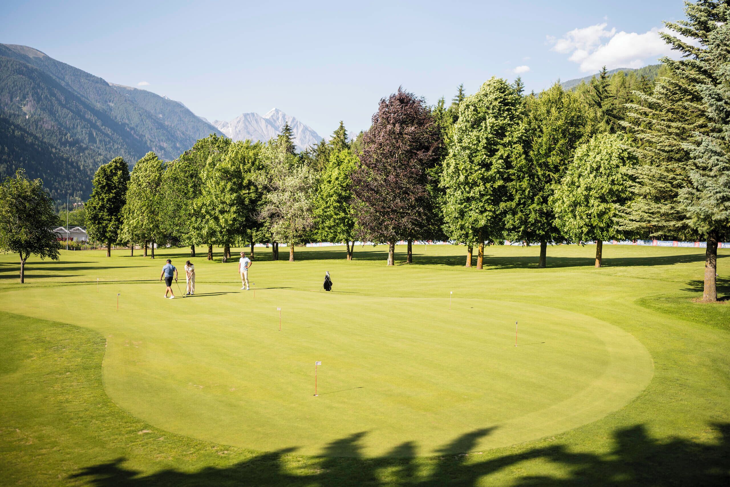 A golf course with a mountainous backdrop, surrounded by trees.
