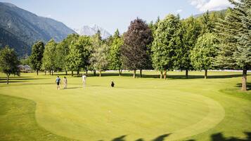 A golf course with a mountainous backdrop, surrounded by trees.