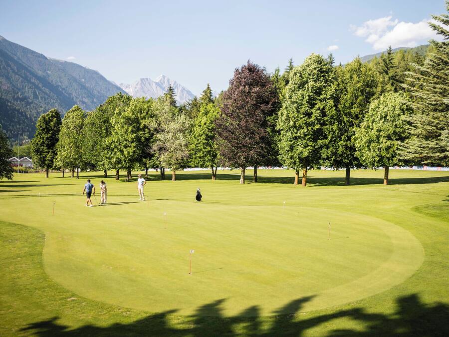 Un campo de golf con montañas al fondo, rodeado de árboles.