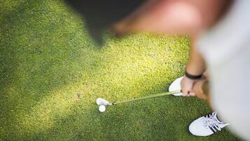 A golf club in motion, a golf ball, and a person's foot on a green surface.