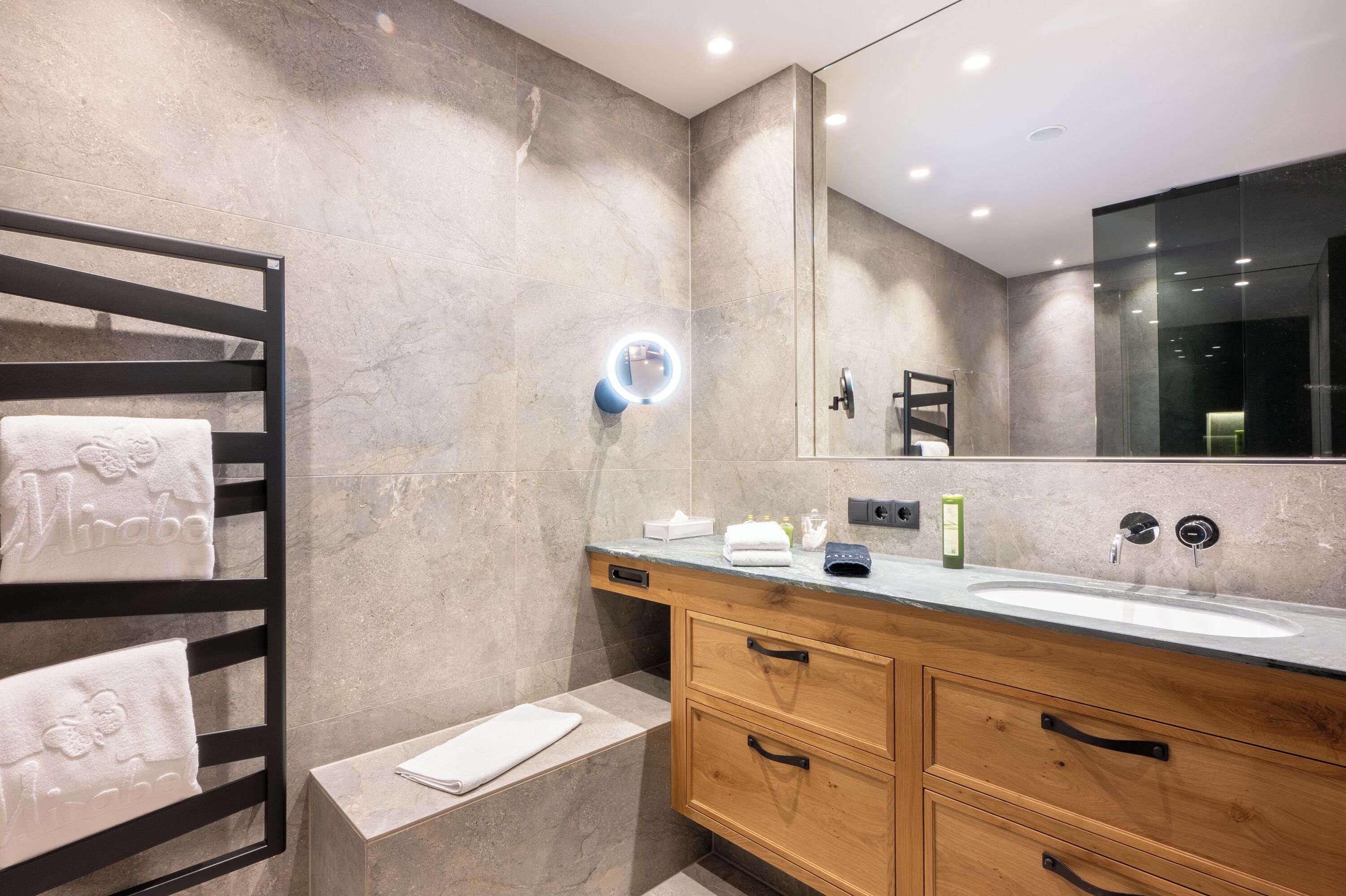 Un baño moderno con pared de mármol, tocador de madera, lavabo y toallero con toallas.