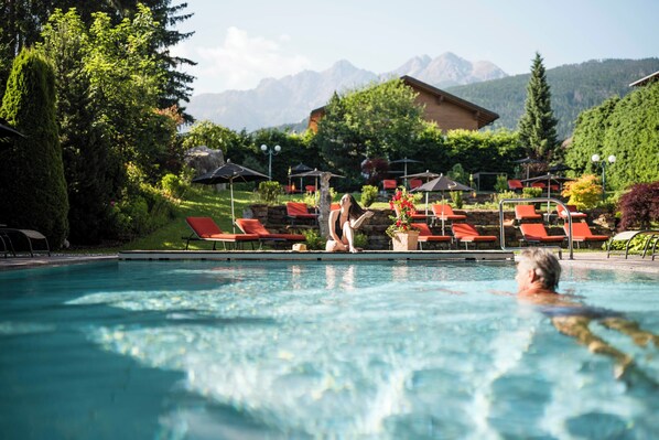 Ein Swimmingpool mit Liegestühlen und Sonnenschirmen, umgeben von Pflanzen und Bergen.
