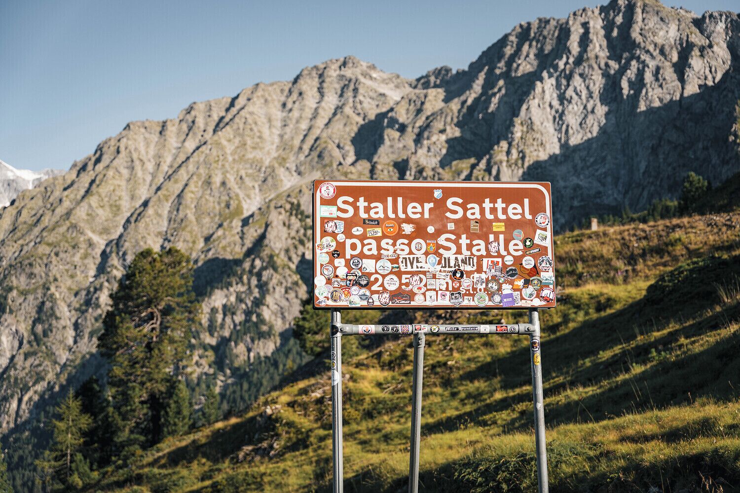 Un letrero con la leyenda 'Staller Sattel' y 'passo Stalle', rodeado de pegatinas.