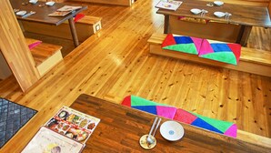 A restaurant with wooden tables and benches, some with colorful cushions. - Sarangbang (Kyoto)