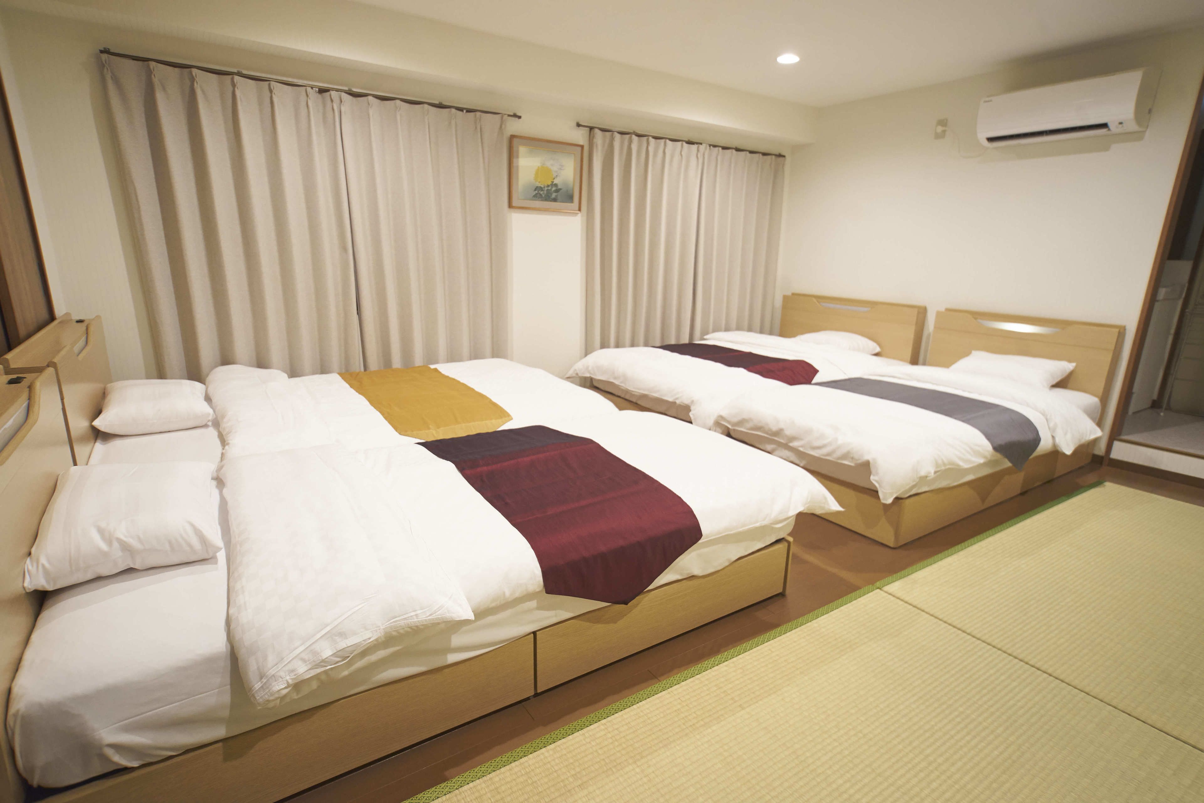 Habitación de hotel con dos camas, un ventanal con cortinas, un aire acondicionado instalado en la pared y un pequeño cuadro en la pared.