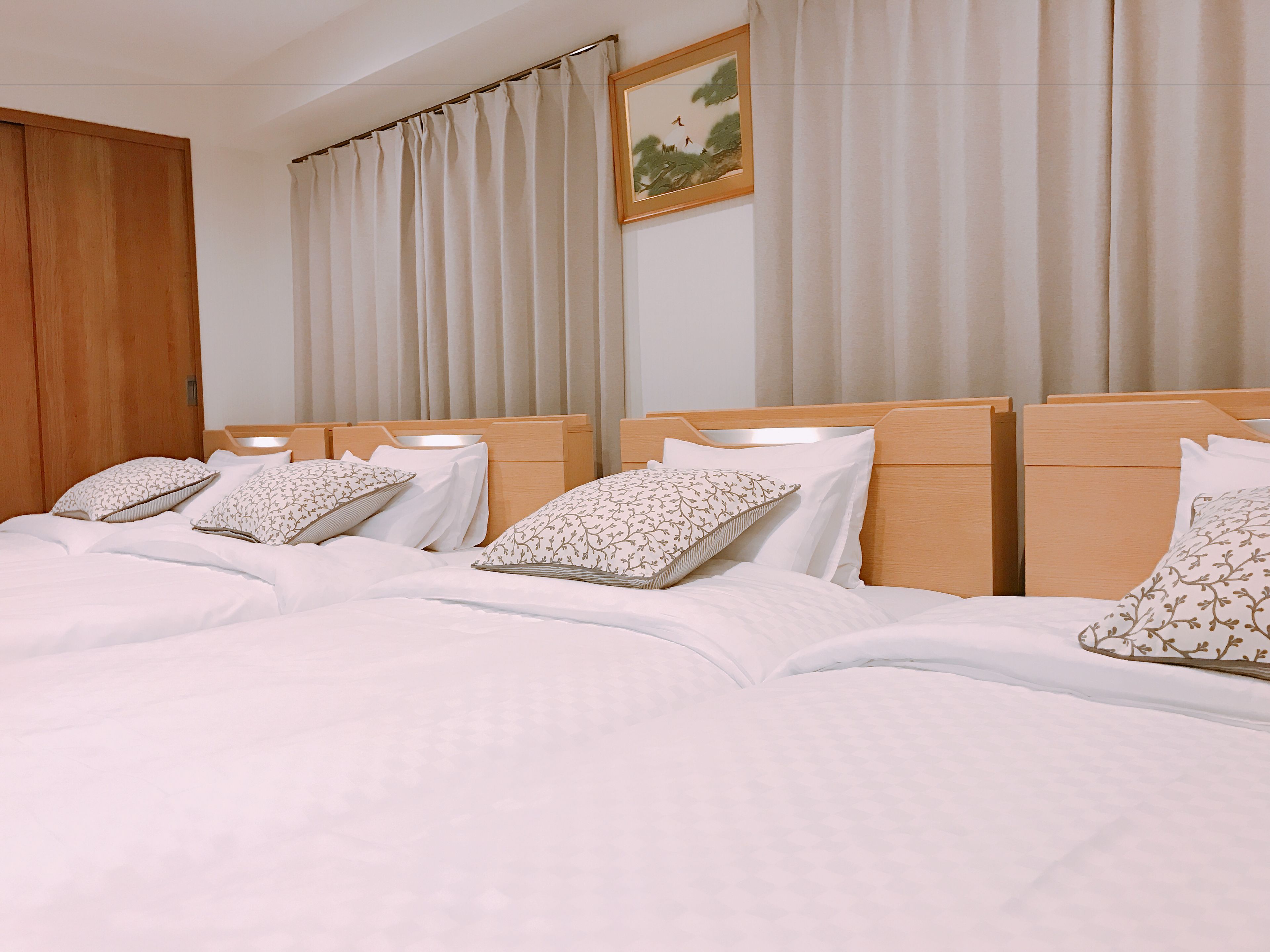 A hotel room with a large bed, multiple pillows, a wooden headboard, and a painting on the wall.