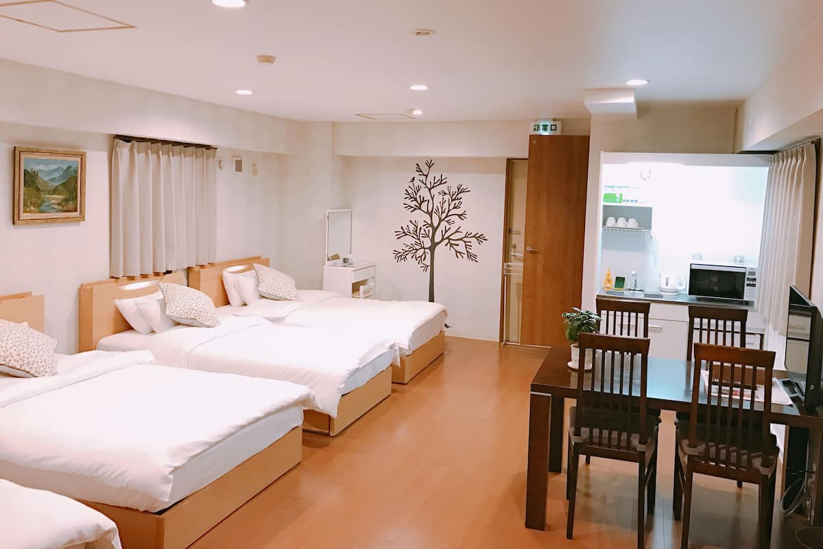 Une chambre d’hôtel avec deux lits, un bureau avec des chaises, une petite kitchenette et une salle de bain visible à travers une porte ouverte.