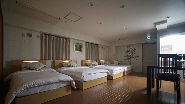 A hotel room with three beds, wooden flooring, and a dining area with a table and chairs. - Sarangbang (Kyoto)