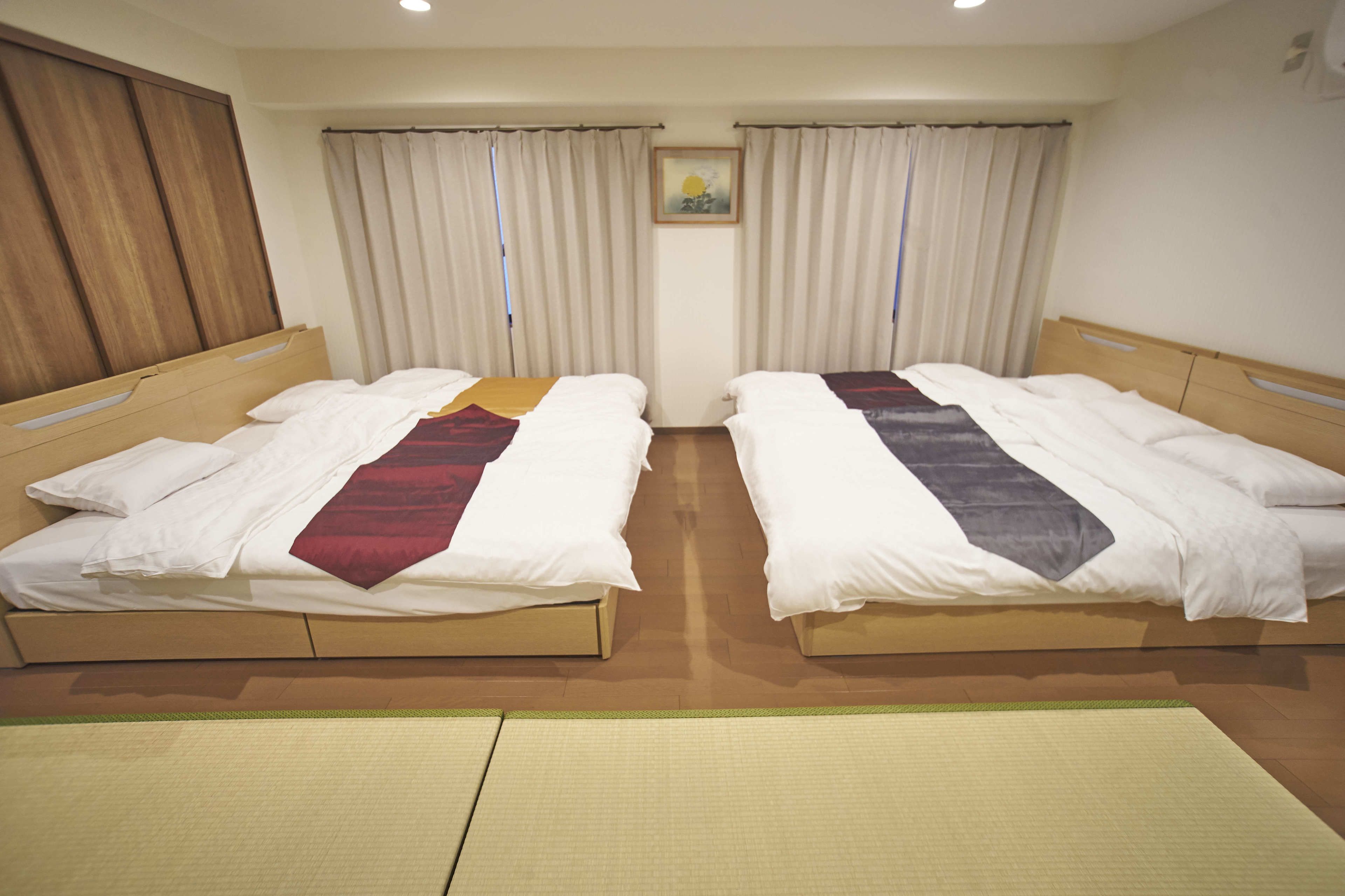 A hotel room with two single beds, a wooden headboard, a large window with curtains, and a tatami mat on the floor.