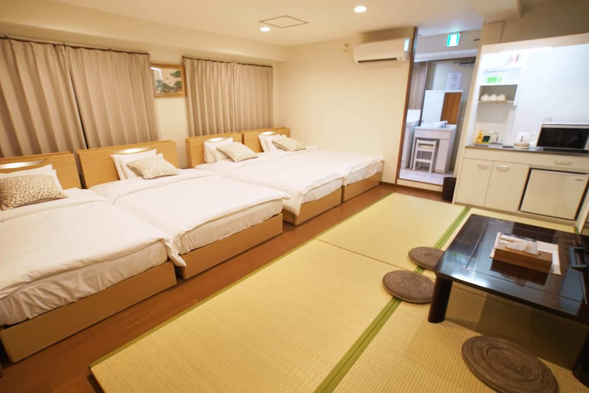 Une chambre d’hôtel avec trois lits, une petite kitchenette et une salle de bain visible à travers une porte coulissante.