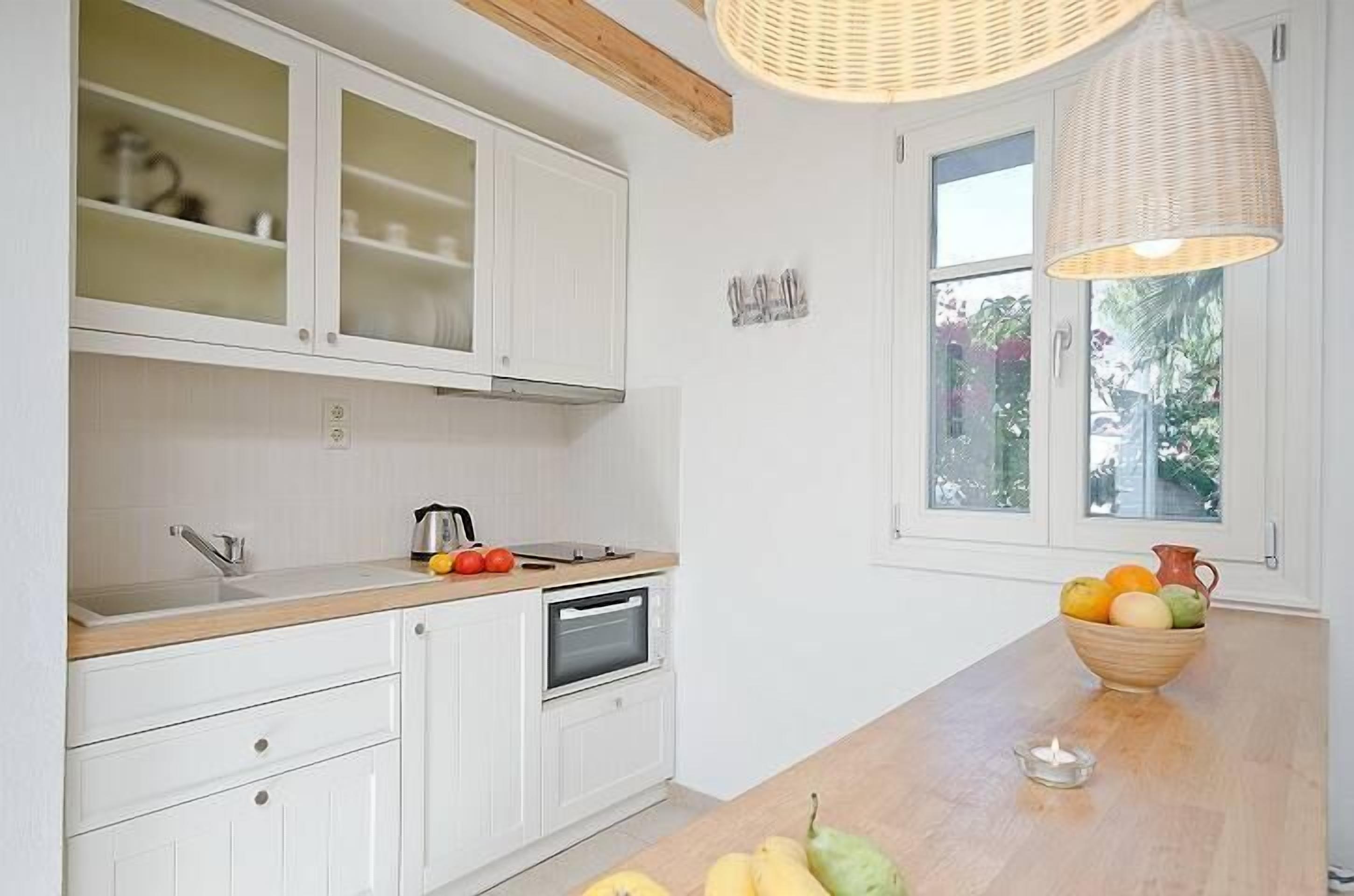 Eine moderne Küche mit weißen Schränken, einer Holz Arbeitsplatte, einem eingebauten Backofen und einem großen Fenster mit Blick auf Grünflächen.