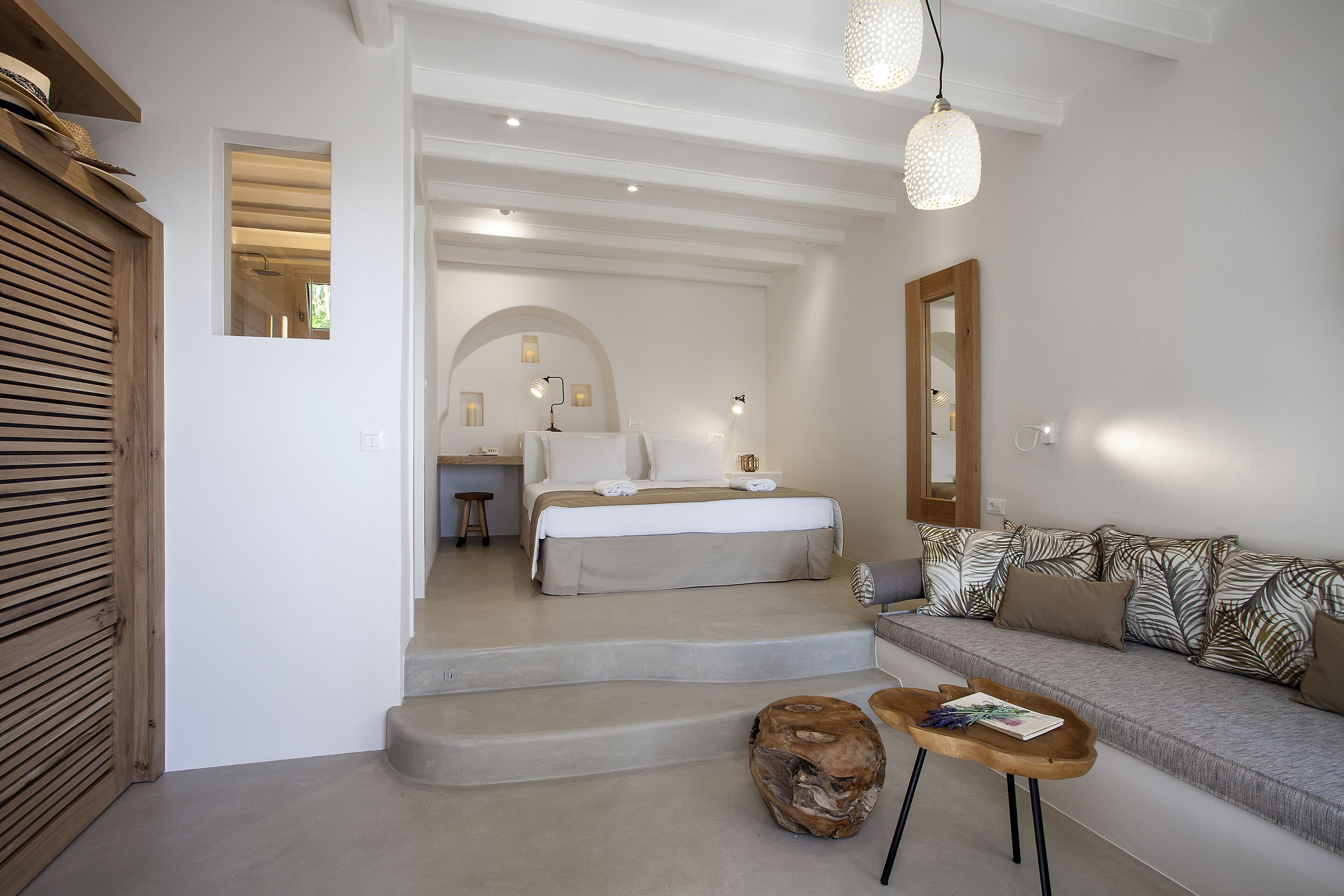 A modern bedroom with a bed, a sofa, and a small table. There are steps leading to another room.