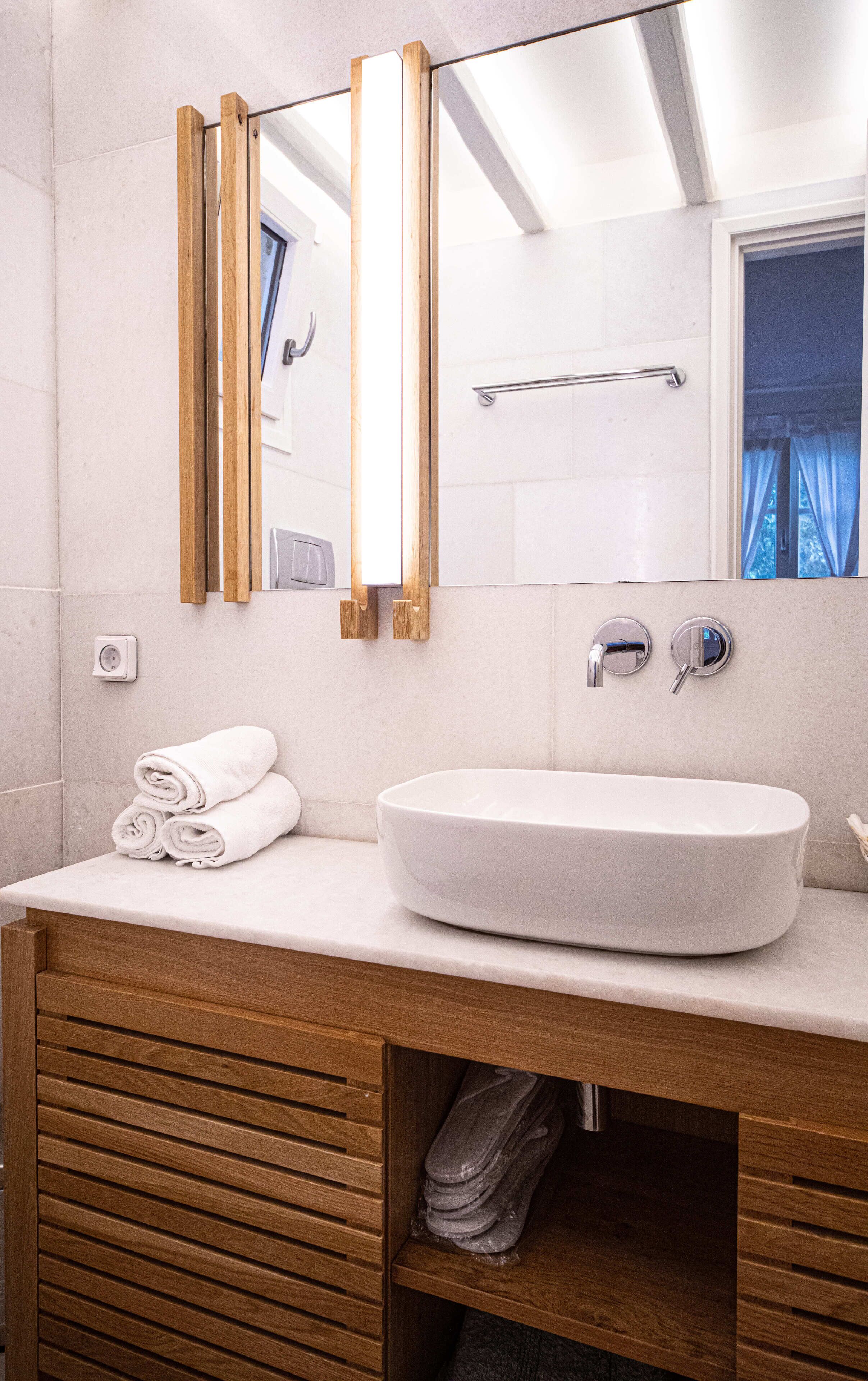 A modern bathroom with a large mirror, a white sink, and wooden cabinetry.