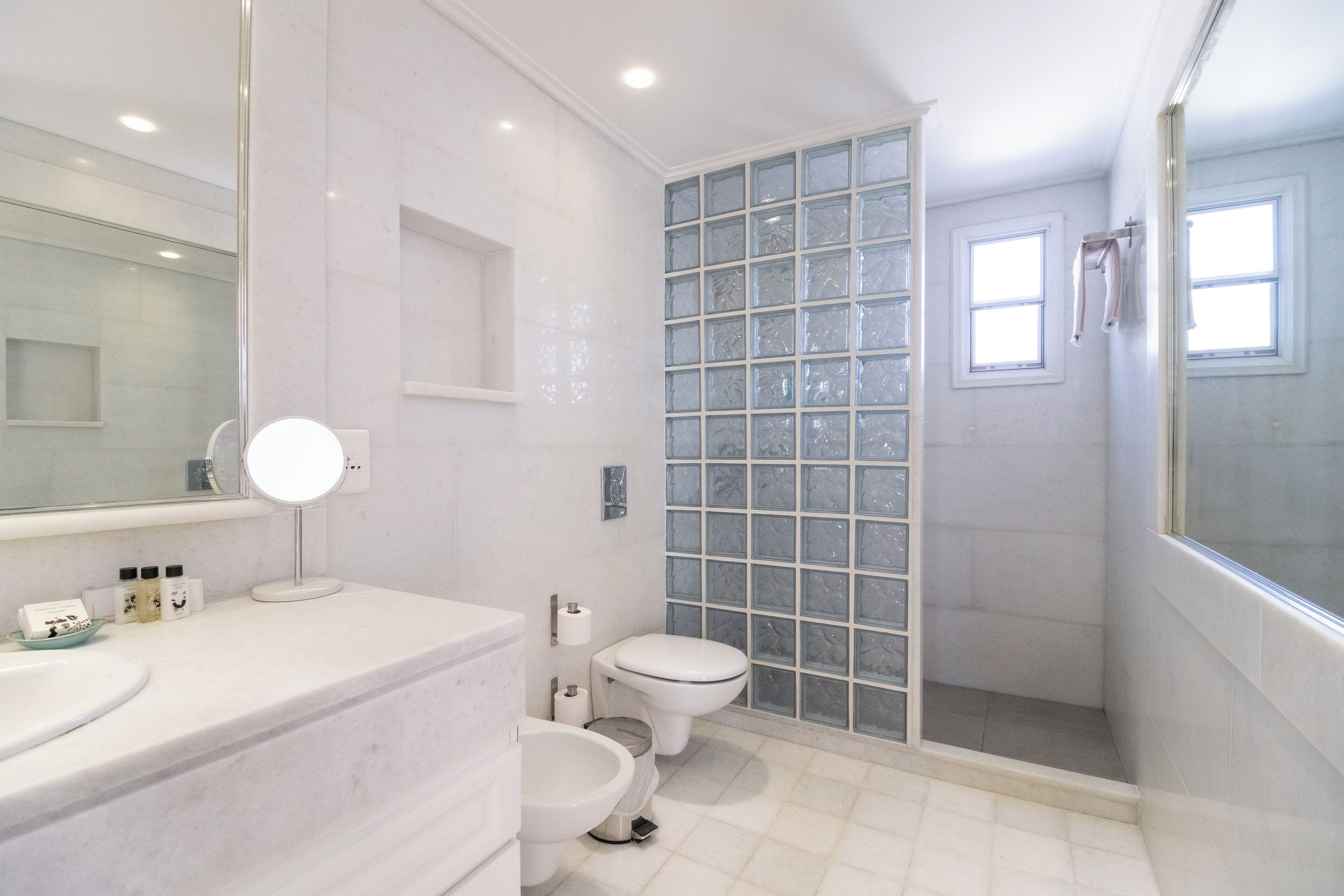 A modern bathroom with a marble vanity, a glass shower enclosure, and a toilet.