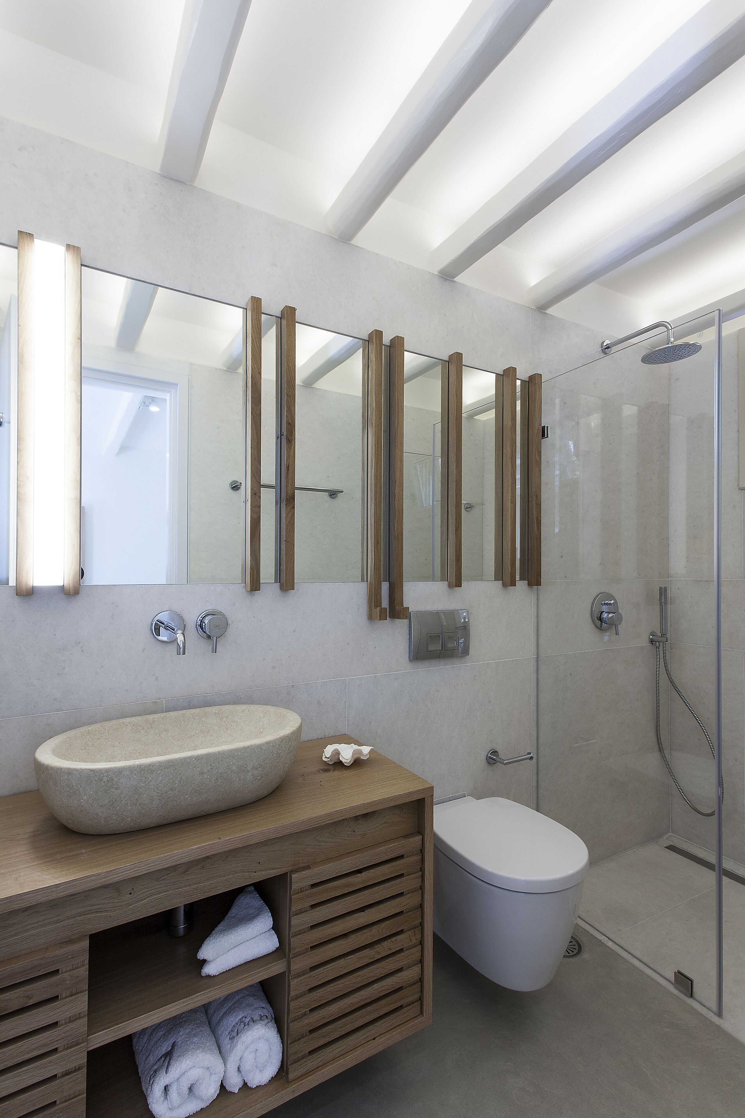 Een moderne badkamer met een grote spiegel, een wastafel op een voetstuk, een toilet en een douche met glazen wanden.