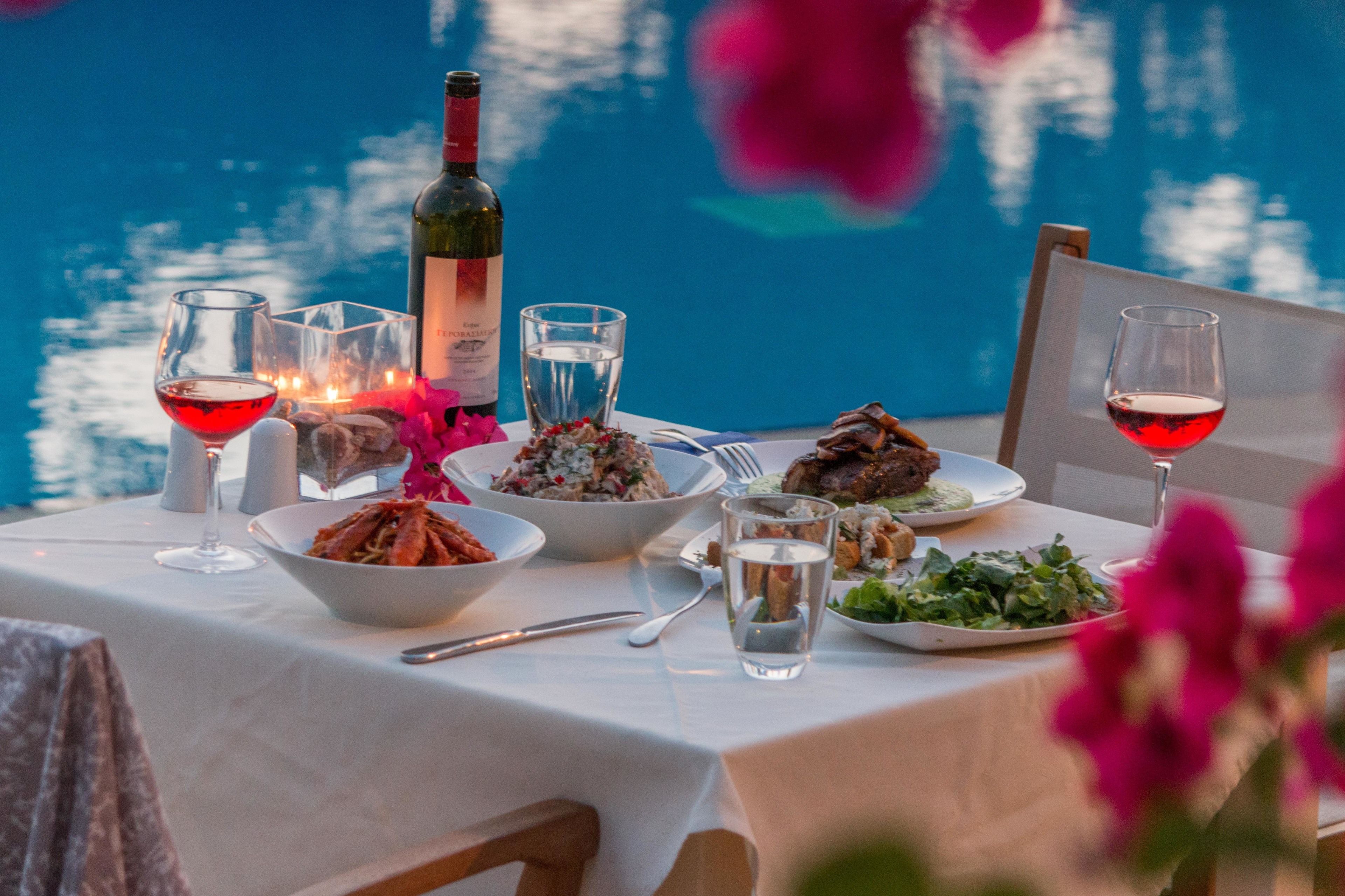 A table set with dinnerware, glasses, and a bottle of wine, with a view of water in the background.