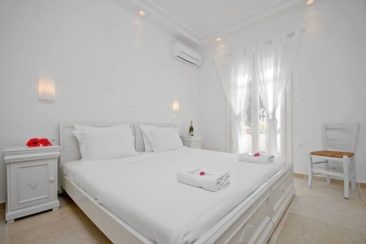 Habitación de hotel con una cama grande, una mesita de noche, una silla y una ventana con cortinas.