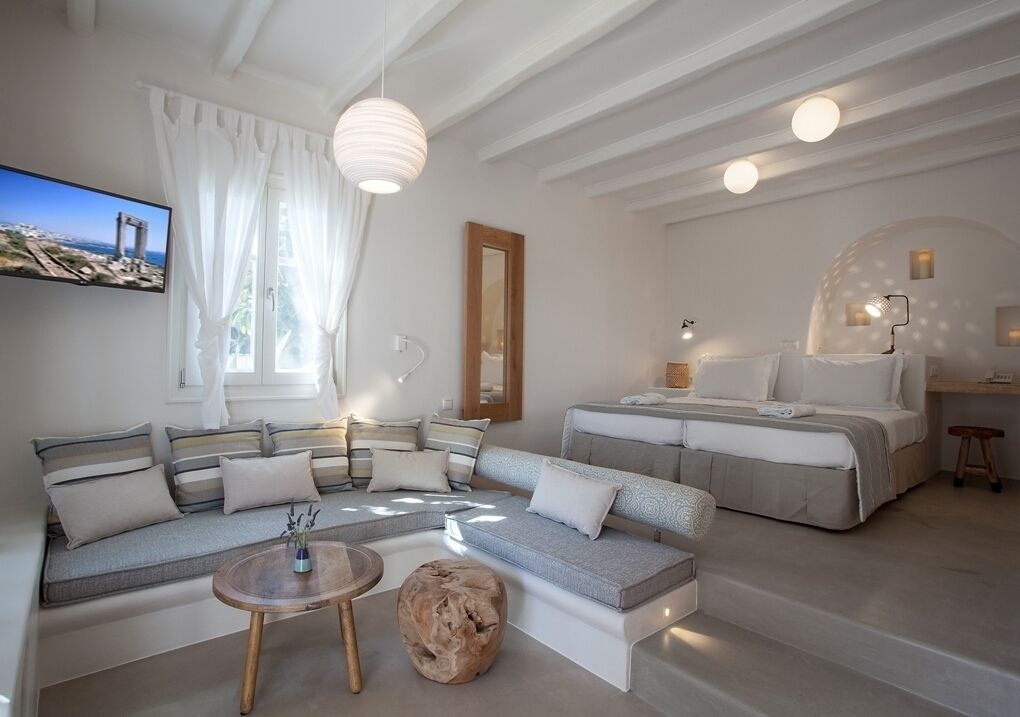 A modern bedroom with a large bed, a sofa, and a TV mounted on the wall.