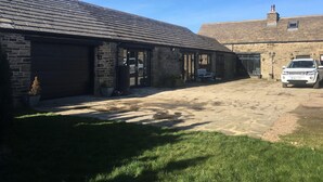 A stone building with a garage, a white car parked in front, and a clear blue sky. - Windy Bank Hall - Holiday Home (Sheffield)