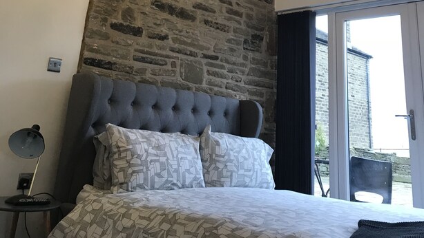 A bedroom with a stone wall, a tufted headboard, a patterned bedspread, and a chandelier. - Windy Bank Hall - Holiday Home (Sheffield)