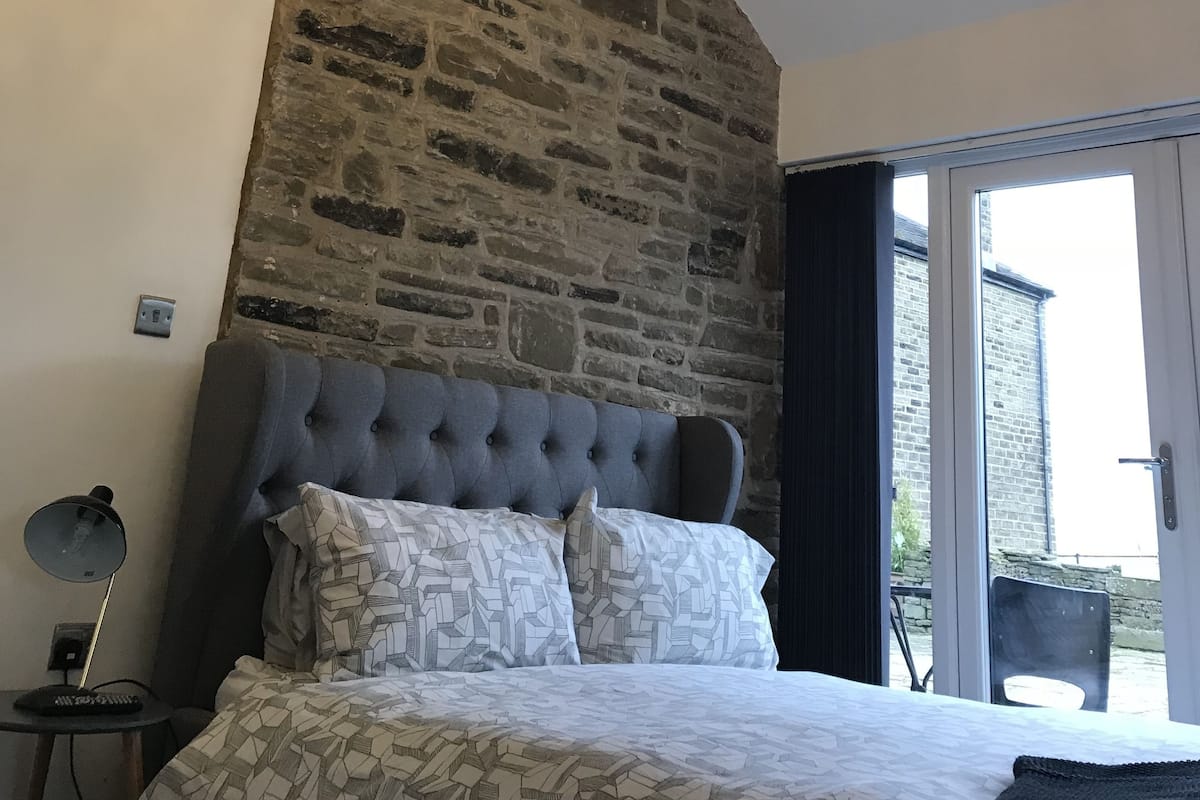A bedroom with a stone wall, a tufted headboard, a patterned bedspread, and a chandelier.