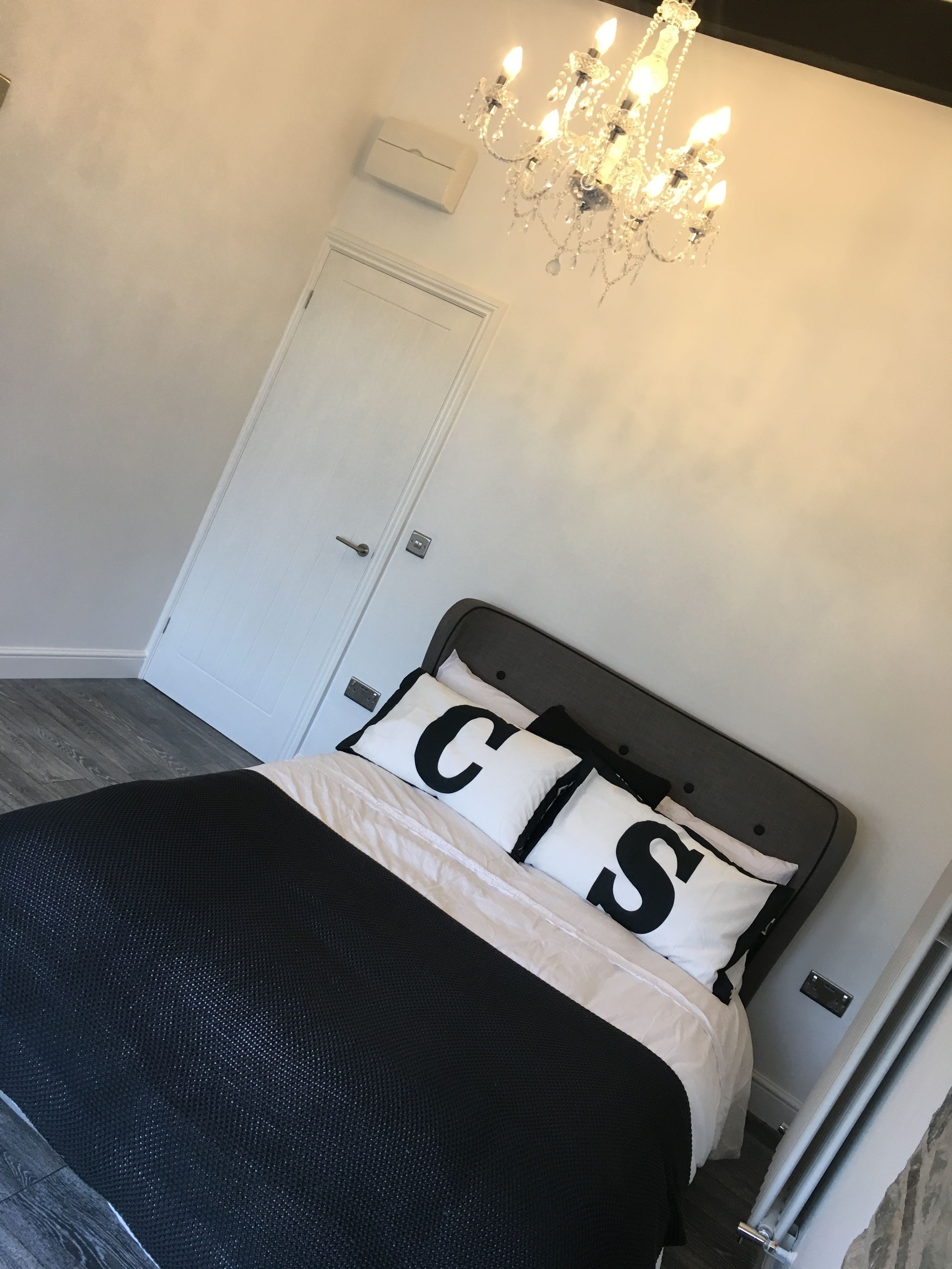 Un dormitorio con cama, candelabro, puerta y un interruptor de luz en la pared.