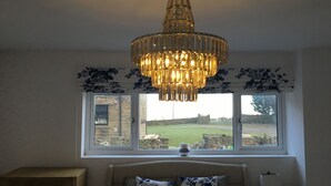A bedroom with a bed, a chandelier, a window with a view of the outdoors, and a bedside table with a lamp and a picture frame. - Windy Bank Hall - Holiday Home (Sheffield)