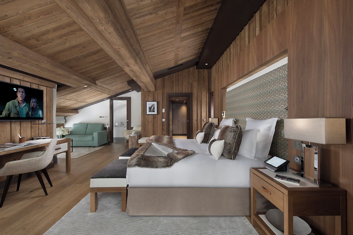 Una habitación de hotel moderna con techo de madera, una cama grande con una manta de piel sintética, un escritorio con silla, un televisor y vistas al exterior.