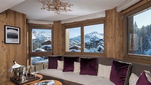 A cozy room with a large window, wooden walls, a cushioned bench, a small table with a tray, and a framed picture.