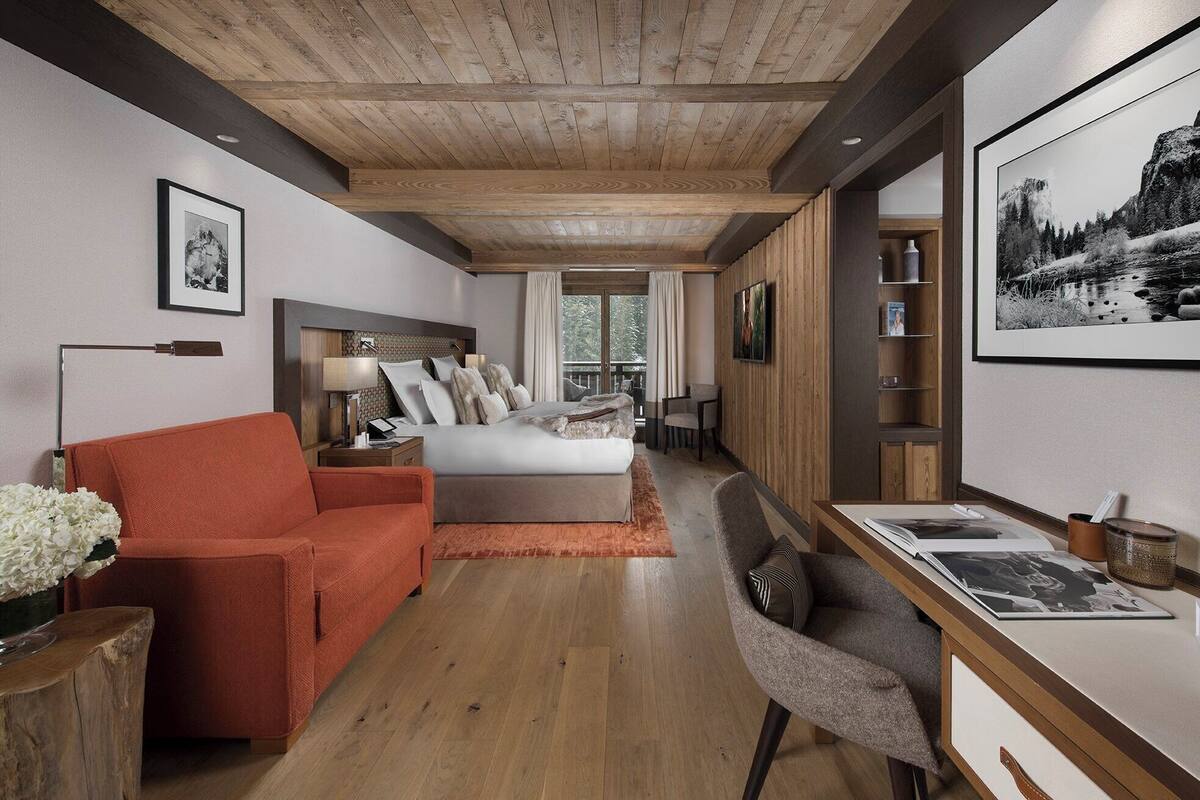 Un dormitorio moderno con techo de madera, una cama grande, un escritorio con silla y vistas a un balcón.