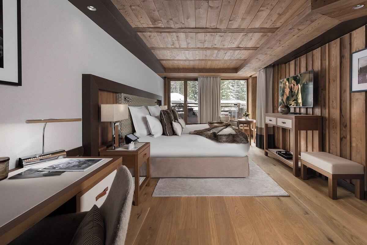 Una habitación moderna y luminosa, con techo de madera, una cama grande, un escritorio con lámpara y un televisor montado en la pared.