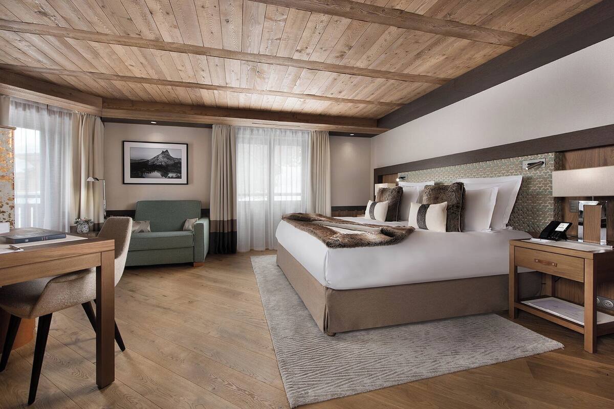 Una habitación de hotel moderna con techo de madera, una cama grande con una manta de piel sintética, un escritorio con una silla y un cuadro en la pared.
