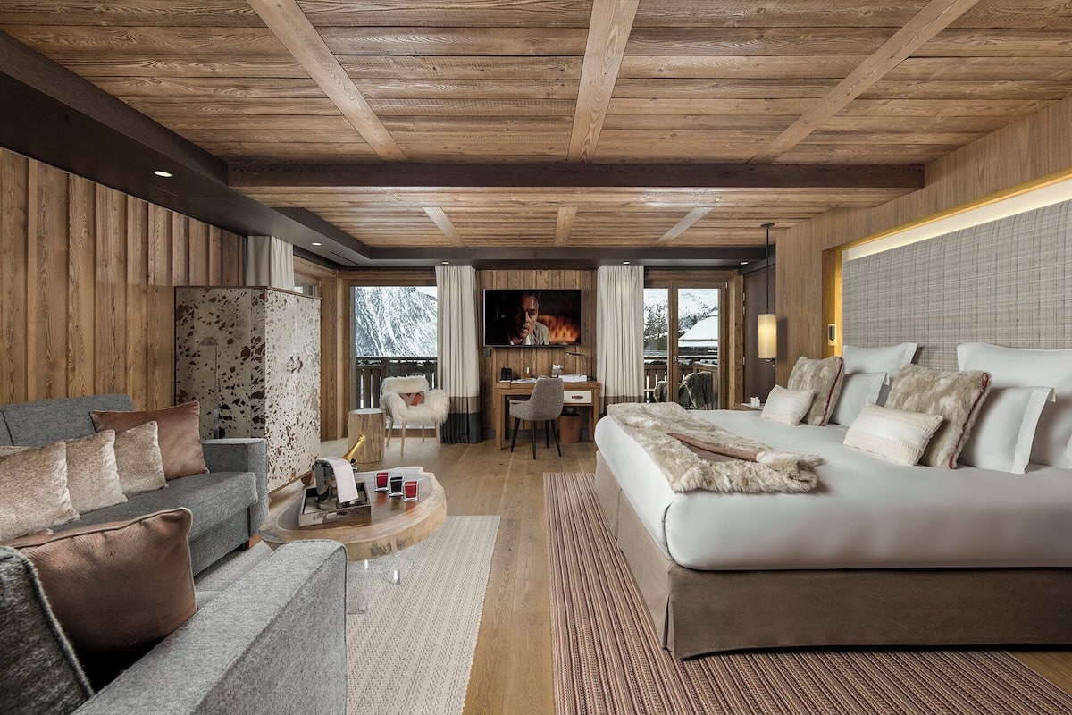 Habitación de hotel moderna con techo de madera, una cama grande, un sofá, un escritorio y vistas al exterior.