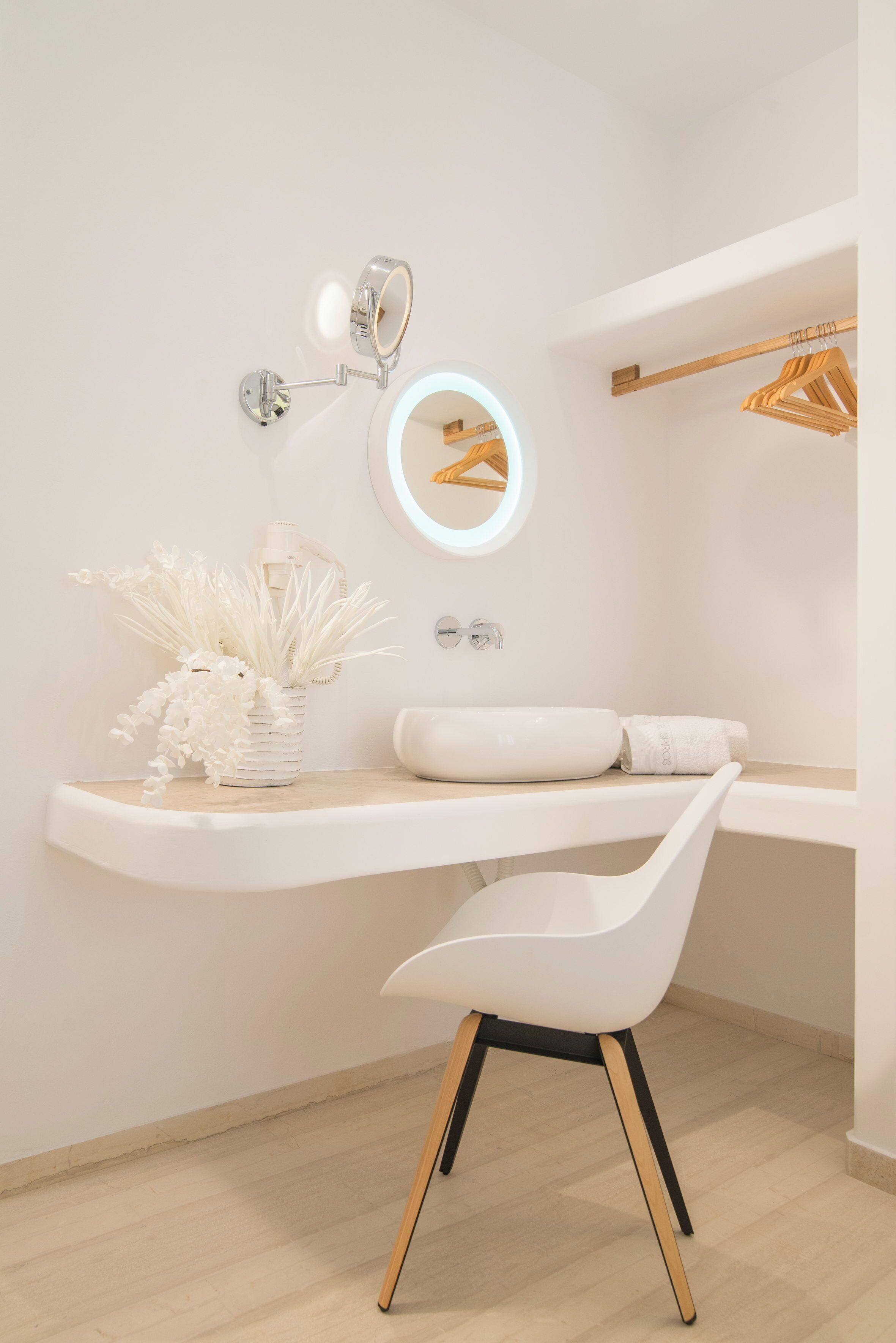 Un baño moderno con tocador, espejo iluminado, silla y perchero.