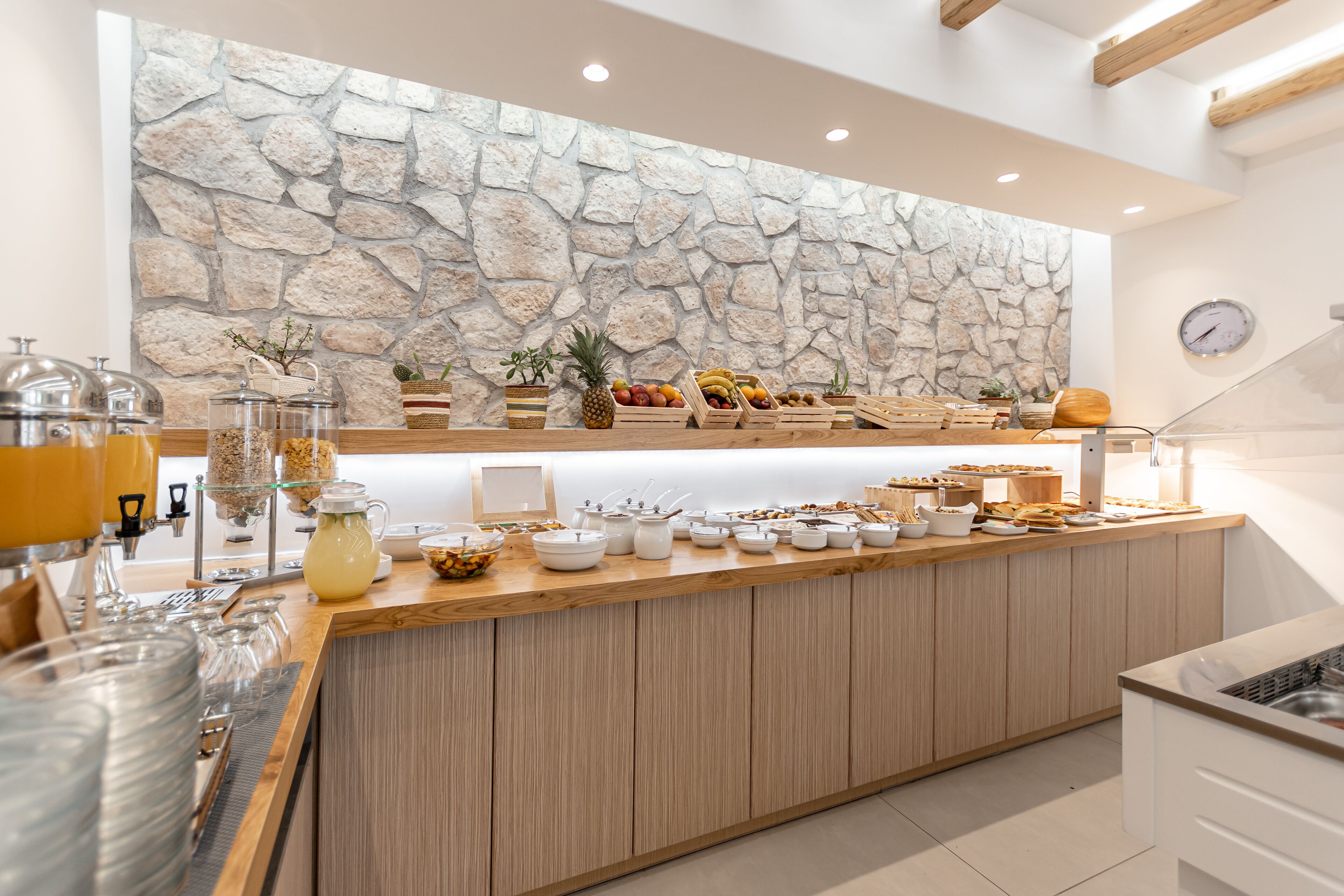 Ein Frühstücksbuffet mit rustikaler Steinwand, Holztresen und verschiedenen Frühstücksangeboten.